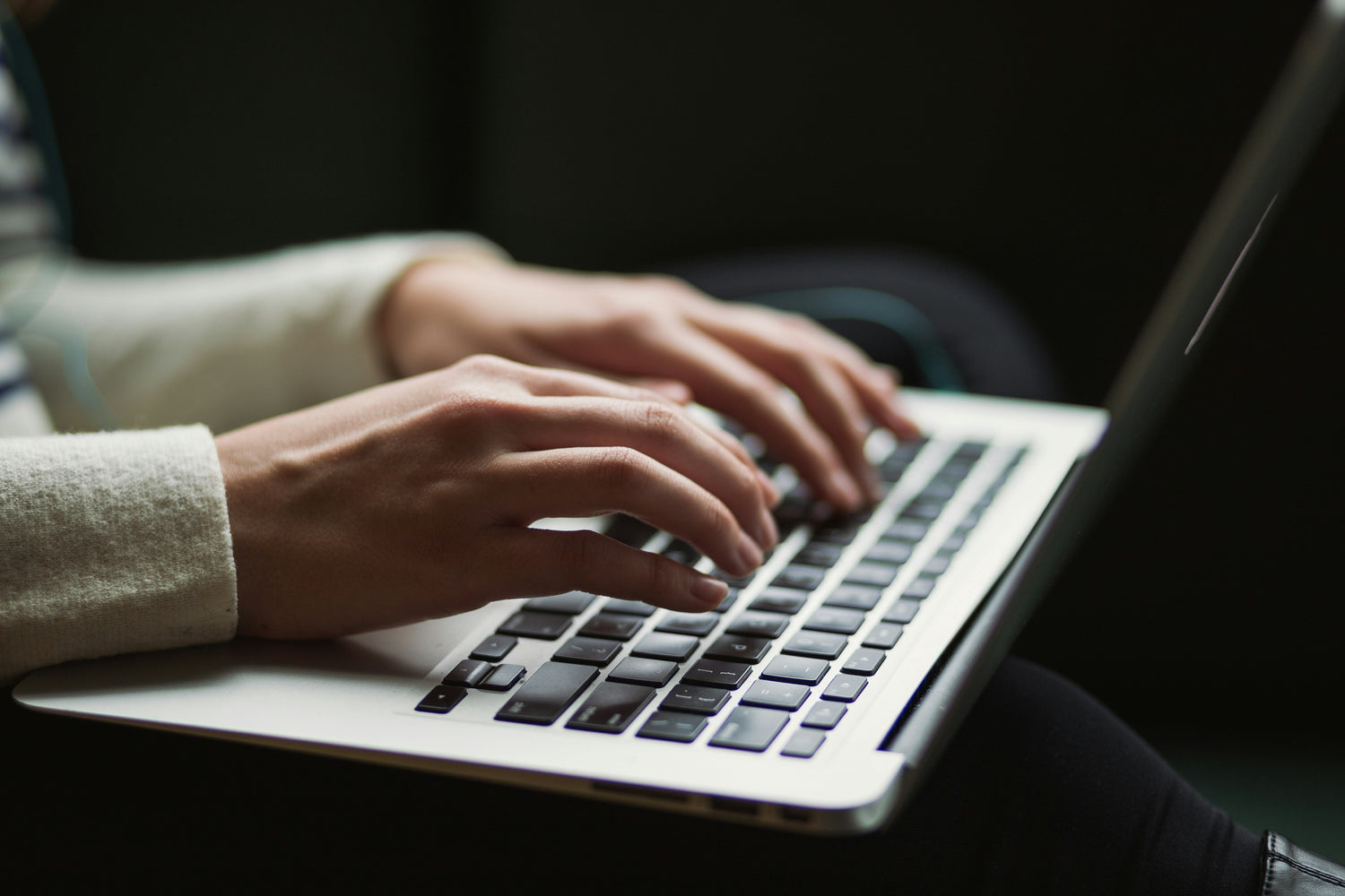 Hands typing on a laptop keyboard, representing the act of writing in a contemporary design context.